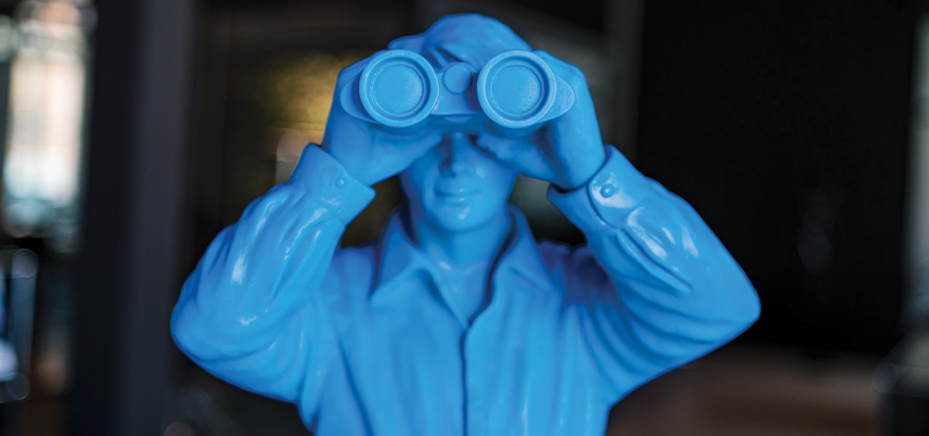 Photo of a blue plastic toy man looking thru binoculars