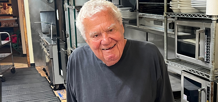 man with white hair smiling in industrial kitchen