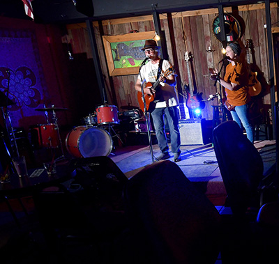 Wide shot of musicians on stage in a dark bar.